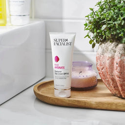 Super Facialist Rosehip Hydrate Day Cream tube on a wooden tray next to a plant