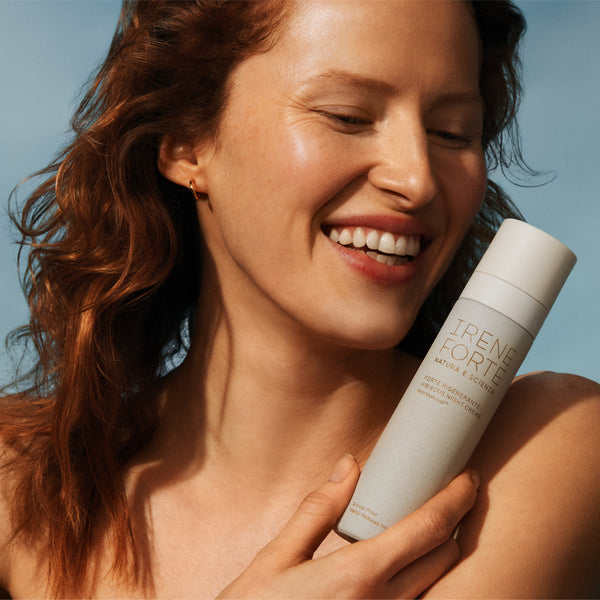 Woman holding a bottle of 'Irene Forte' product against a clear blue sky.