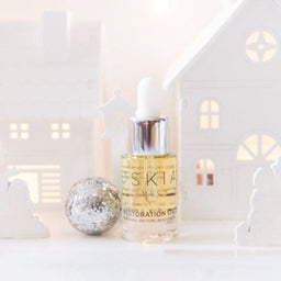 OSKIA Restoration Oil Travel bottle in front of christmas houses