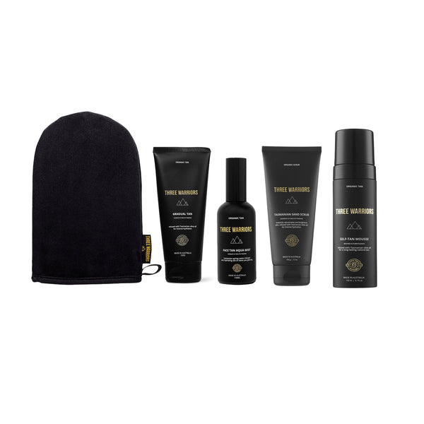 A set of five black haircare products from Three Warriors, including a towel, shampoo, conditioner, hair oil, and hair mask, arranged on a plain white background.