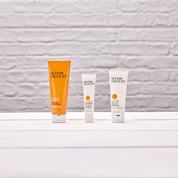 Vitamin C daily polish wash next to eye cream next to daily moisturiser on white wooden table and white brick wall