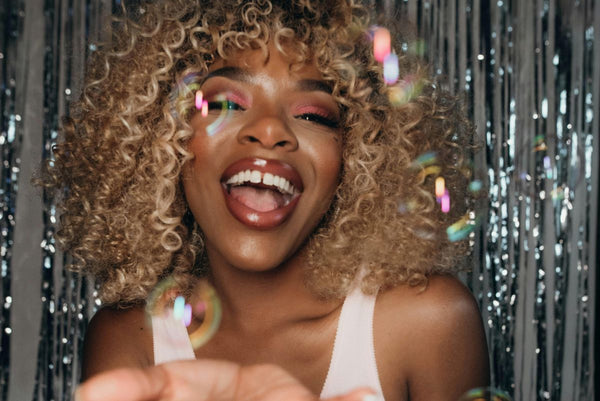 woman with curly hair laughing surrounded by rainbow bubbles