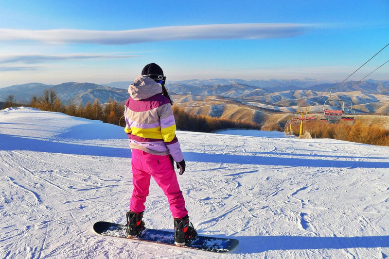 woman in colourful snow suit on a snowboard looking over the slopes
