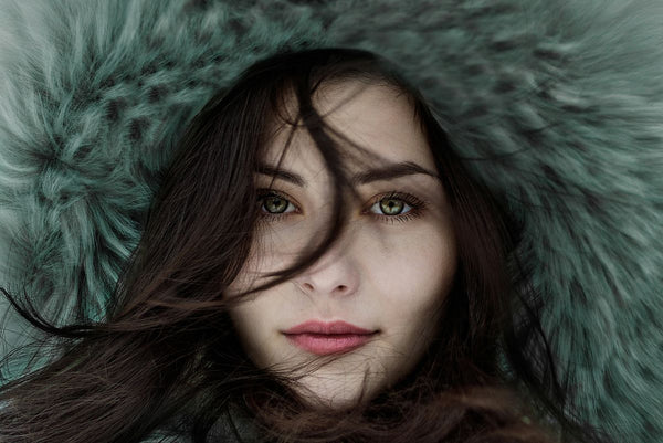 close up of woman's face wearing a fur hat with dark hair across her face