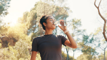 A woman drinking a glass of water with trees in the background.