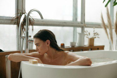 woman in a bath with a bar of soap infront of her, looking to the side