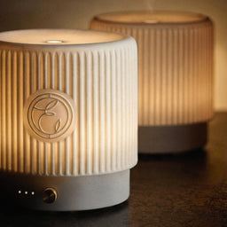 Two textured ceramic lamps with a brand logo on a dark surface