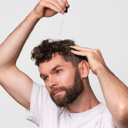Man applying a dropper of liquid to his hair against a white background