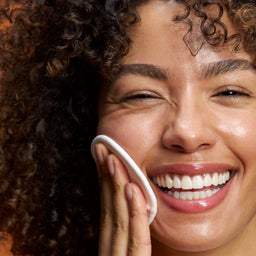 Woman applying a skincare product to her face with a brown background