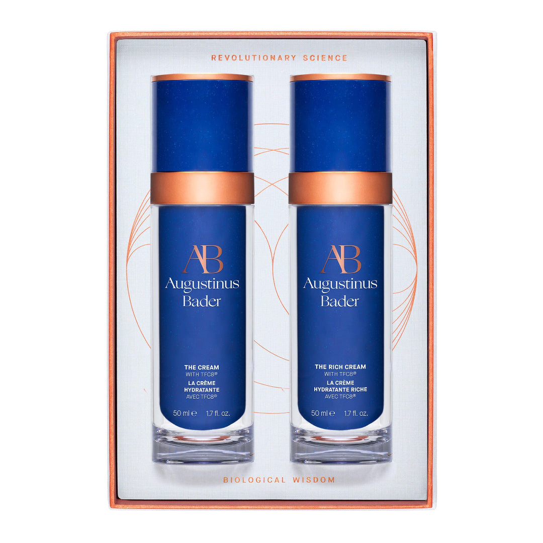 Two blue skincare bottles with bronze accents in a decorative box, featuring the brand 'Augustinus Bader'.