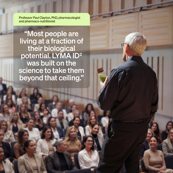 A man in a black shirt stands at the front of a lecture hall addressing a large audience, with a semi-transparent text box containing a quote attributed to Professor Paul Clayton, PhD.