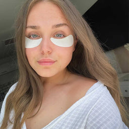 Woman with eye patches on her face, wearing a white top.