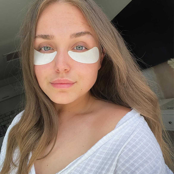 Woman with eye patches on her face, wearing a white top.