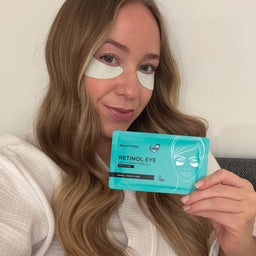 Woman holding a box of BeautyPro Retinol Eye patches with eye patches on her face.