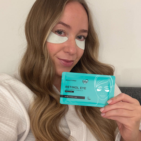 Woman holding a box of BeautyPro Retinol Eye patches with eye patches on her face.
