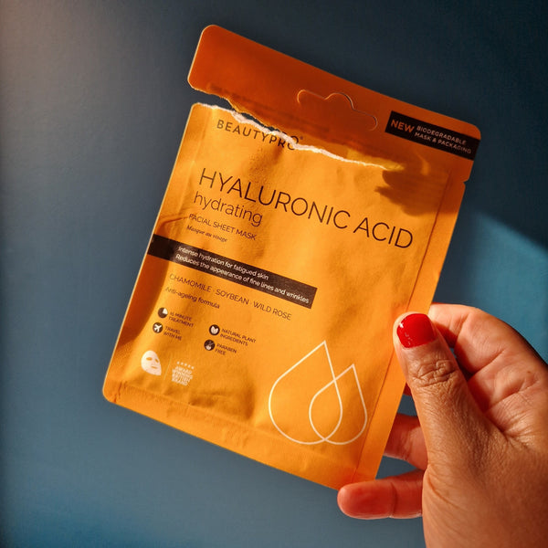 Hand holding a BeautyPro hyaluronic acid mask package against a blue background