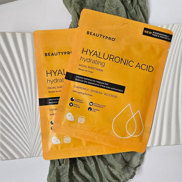 Two yellow BeautyPro hyaluronic acid facial sheet masks on a textured surface.