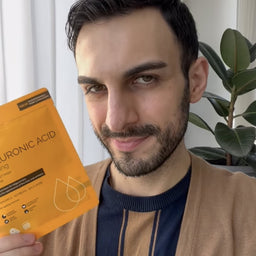 Man holding a package of hyaluronic acid mask with a plant in the background