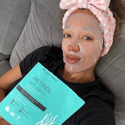 Person with a facial mask on holding a BeautyPro retinol anti-aging product package.