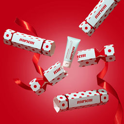Several Mirren-branded cosmetic tubes and boxes with red polka dots and red ribbons floating against a solid red background.