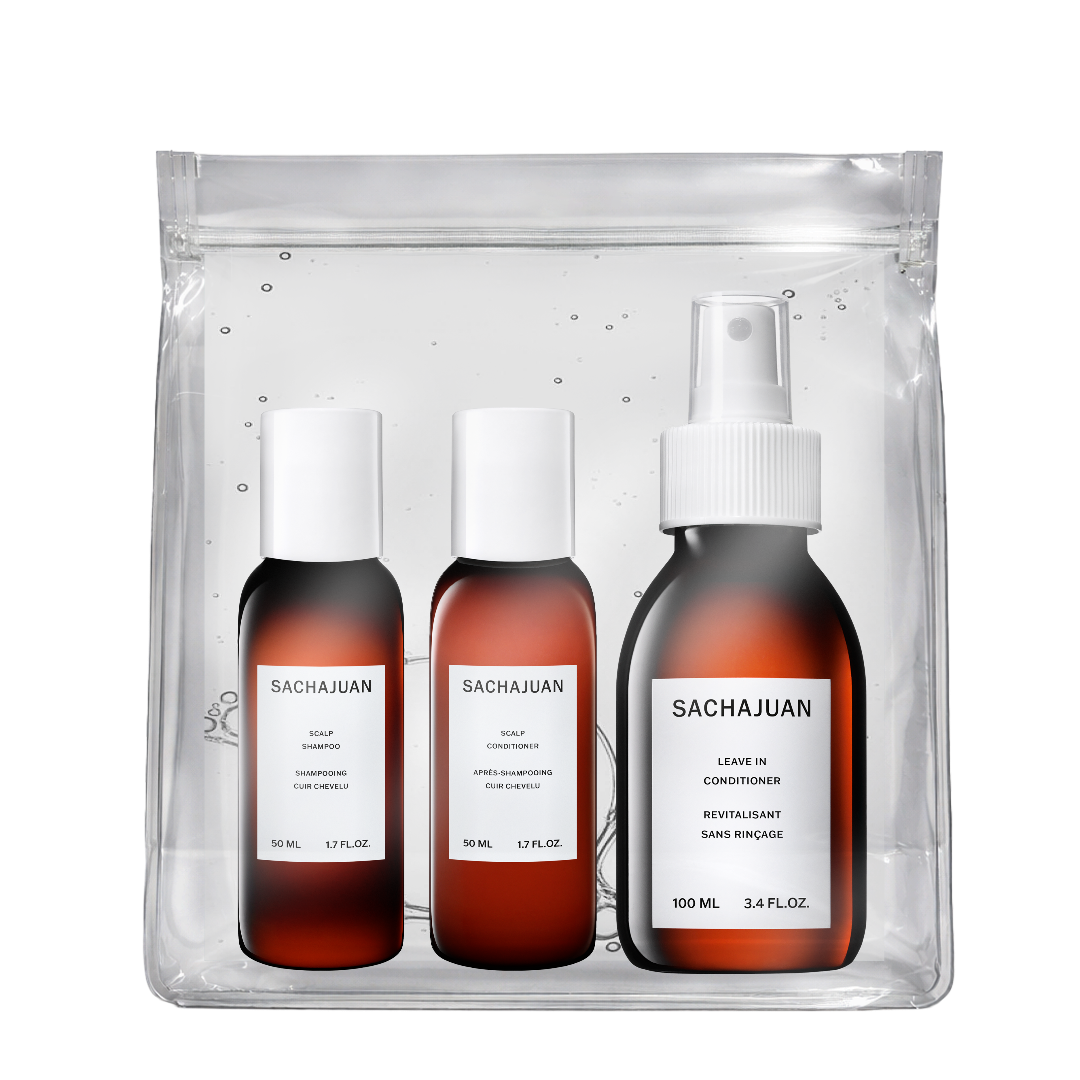 A Sachajuan hair care set in a clear resealable pouch, containing three amber bottles with white caps: conditioner, leave-in conditioner, and moisturizing hair primer, on a white background.