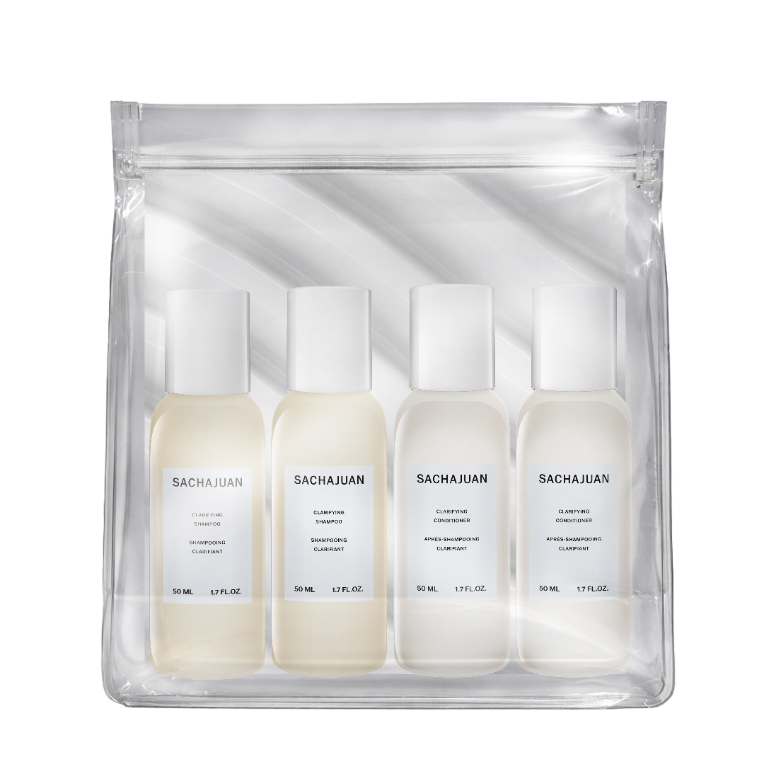 A clear zip pouch containing four small white bottles of Sacha Juan haircare products, photographed on a clean white background.