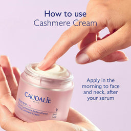A hand scoops cream from a jar of Caudalie Paris Cashmere Cream, held in another hand, with instructional text on a light lavender background.