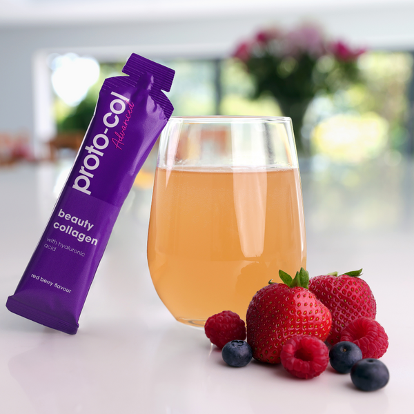 Proto-Col Beauty Collagen in a glass with fruit in front of the glass