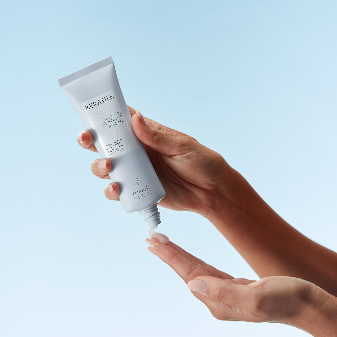 Hand holding a tube of KeraSilk hair care product against a light blue background