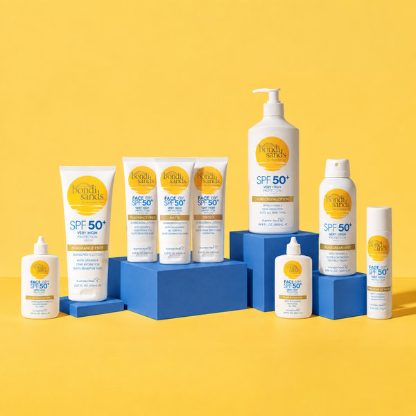 A Keen's Skins SPF 50+ sunscreen product lineup arranged on blue display blocks against a bright yellow background. The set includes a pump bottle, squeeze tubes, a spray can, and a small bottle, all in white packaging with yellow and blue branding.