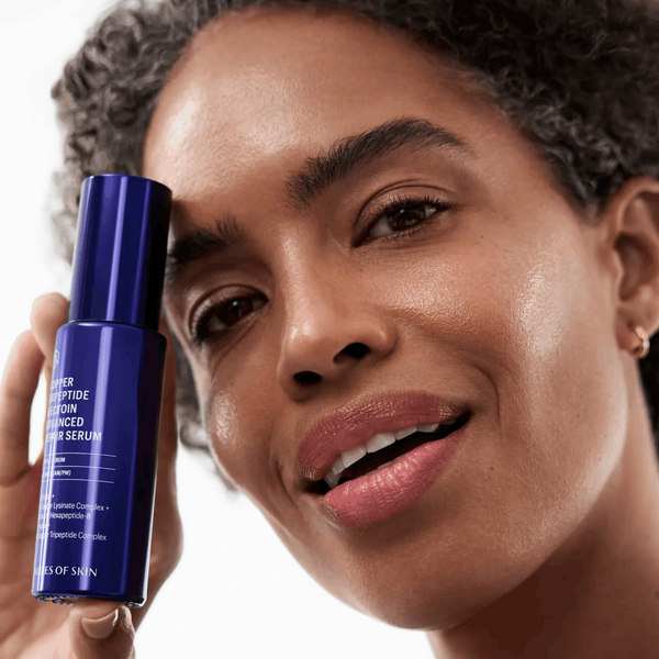 Woman holding a blue skincare serum bottle against a white background