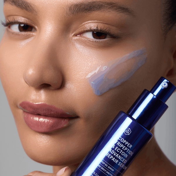Woman holding a blue skincare serum bottle with a gray background