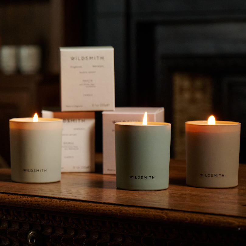 Three lit candles with 'Wildsmith' branding on a wooden surface.