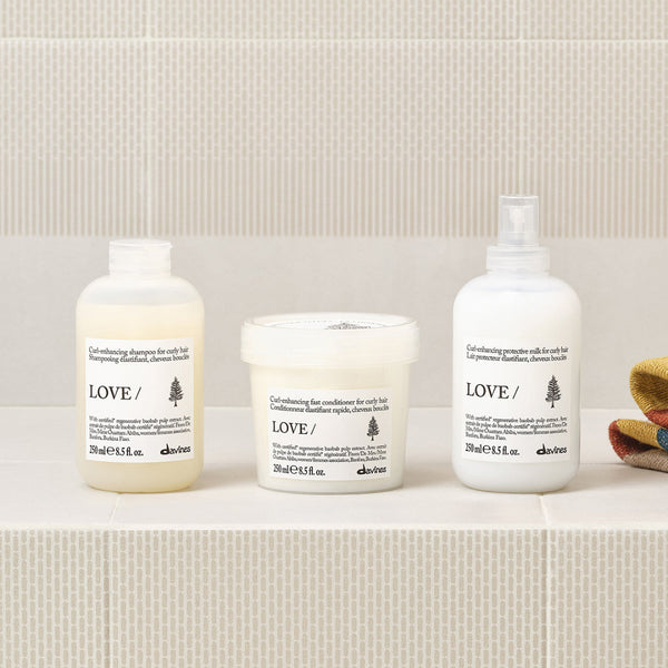 Three white haircare containers from the brand aloves, labeled LOVE, arranged on a light textured surface against a neutral background.