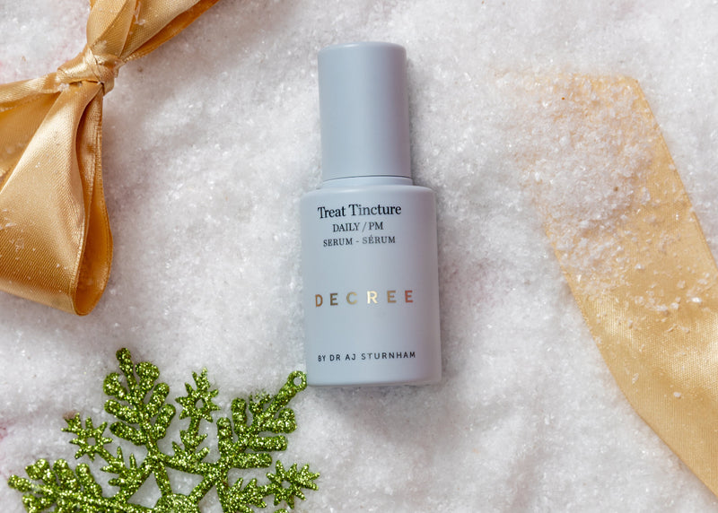 Skincare bottle with gold ribbons and a green decorative snowflake on a textured surface