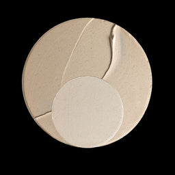 A circular makeup sponge or applicator pad in a warm beige tone, shown against a solid black background.