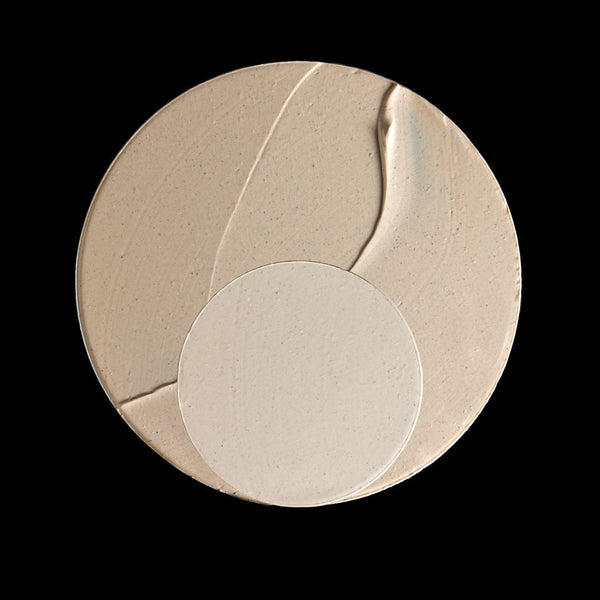 A circular makeup sponge or applicator pad in a warm beige tone, shown against a solid black background.