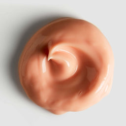 Close-up of peach-colored cream with a swirl on a light gray background