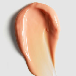 A glossy smear of peachy beige cosmetic cream or foundation on a light gray background.