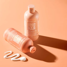Two bottles of hair care product on a peach background