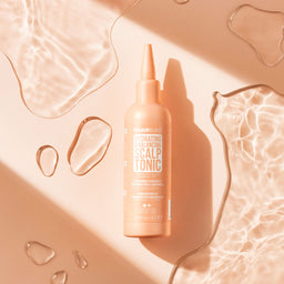 Hairburst scalp tonic bottle on a beige background with water droplets