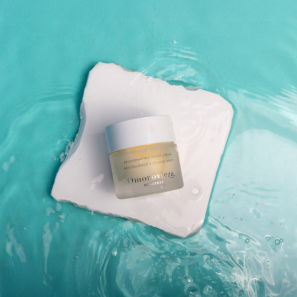 Omorovicza cream jar on a white square with water droplets on a teal background