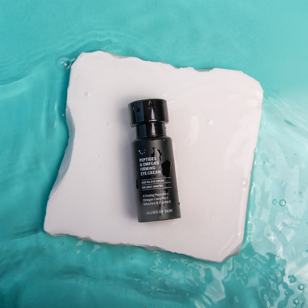 Black eye cream bottle on a white square of cotton with a teal water background