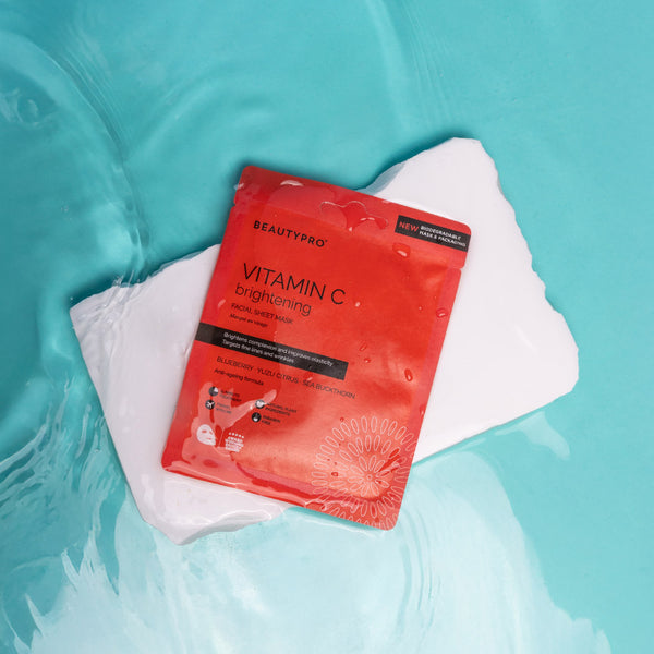 Red BeautyPro vitamin C brightening sheet mask on a white towel with a blue water background