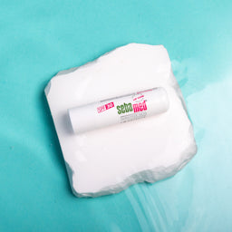 Tube of Sebamed cream on a white square with water droplets against a teal background