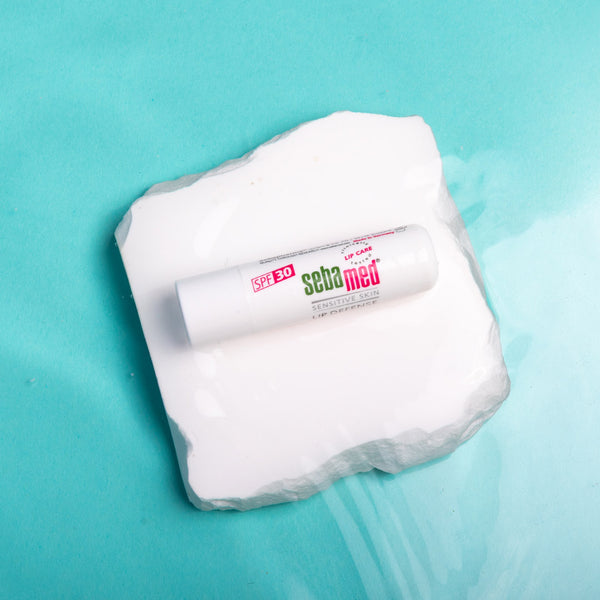 Tube of Sebamed cream on a white square with water droplets against a teal background