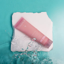 Pink Caudalie skincare product on a white towel with water splashes on a teal background
