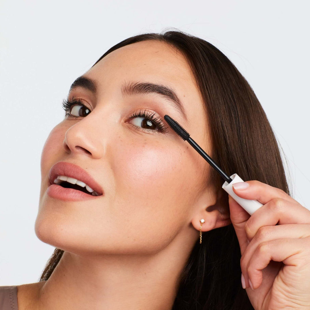 Woman applying mascara to her eyelashes with a white background