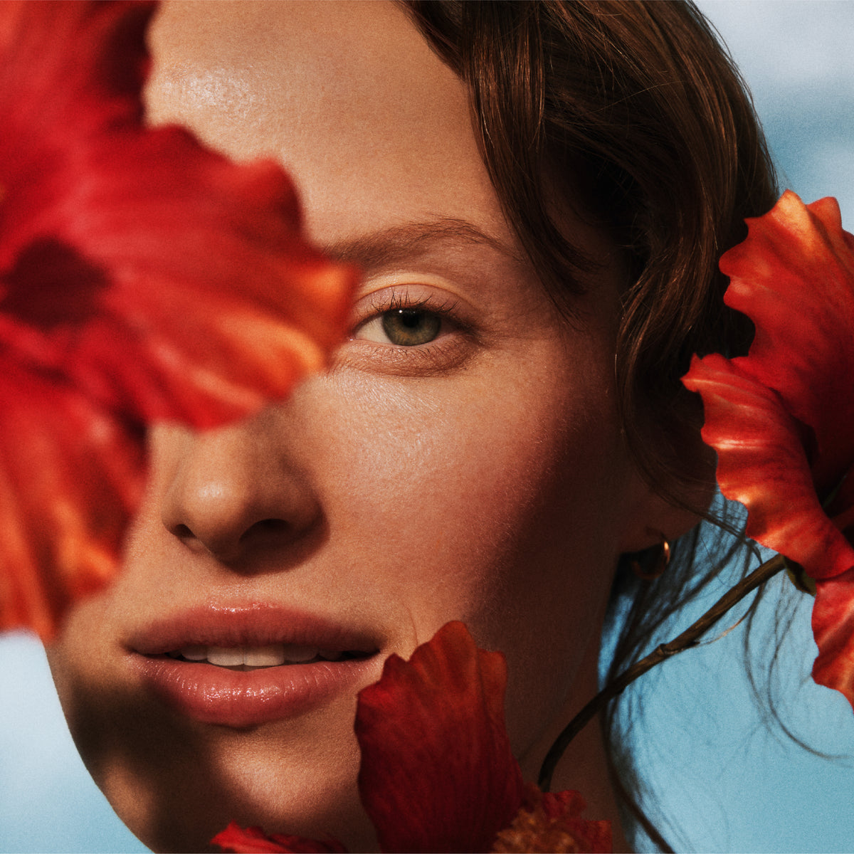 Close-up of a person with red flowers in front of their face, wearing a blue top.