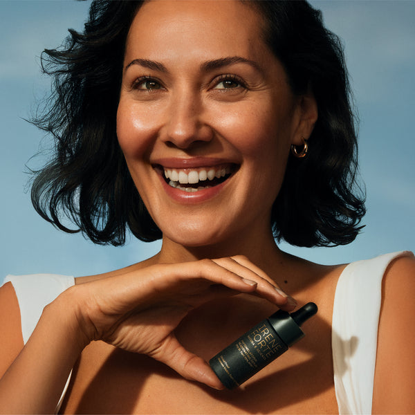 Woman holding a skincare bottle against a blue sky background